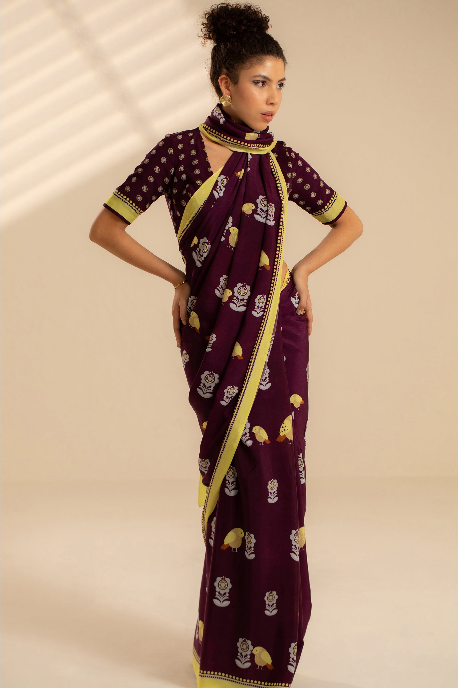 Woman wearing a purple saree with yellow patterns on a beige background