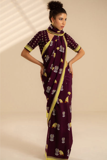 Woman wearing a purple saree with yellow patterns on a beige background